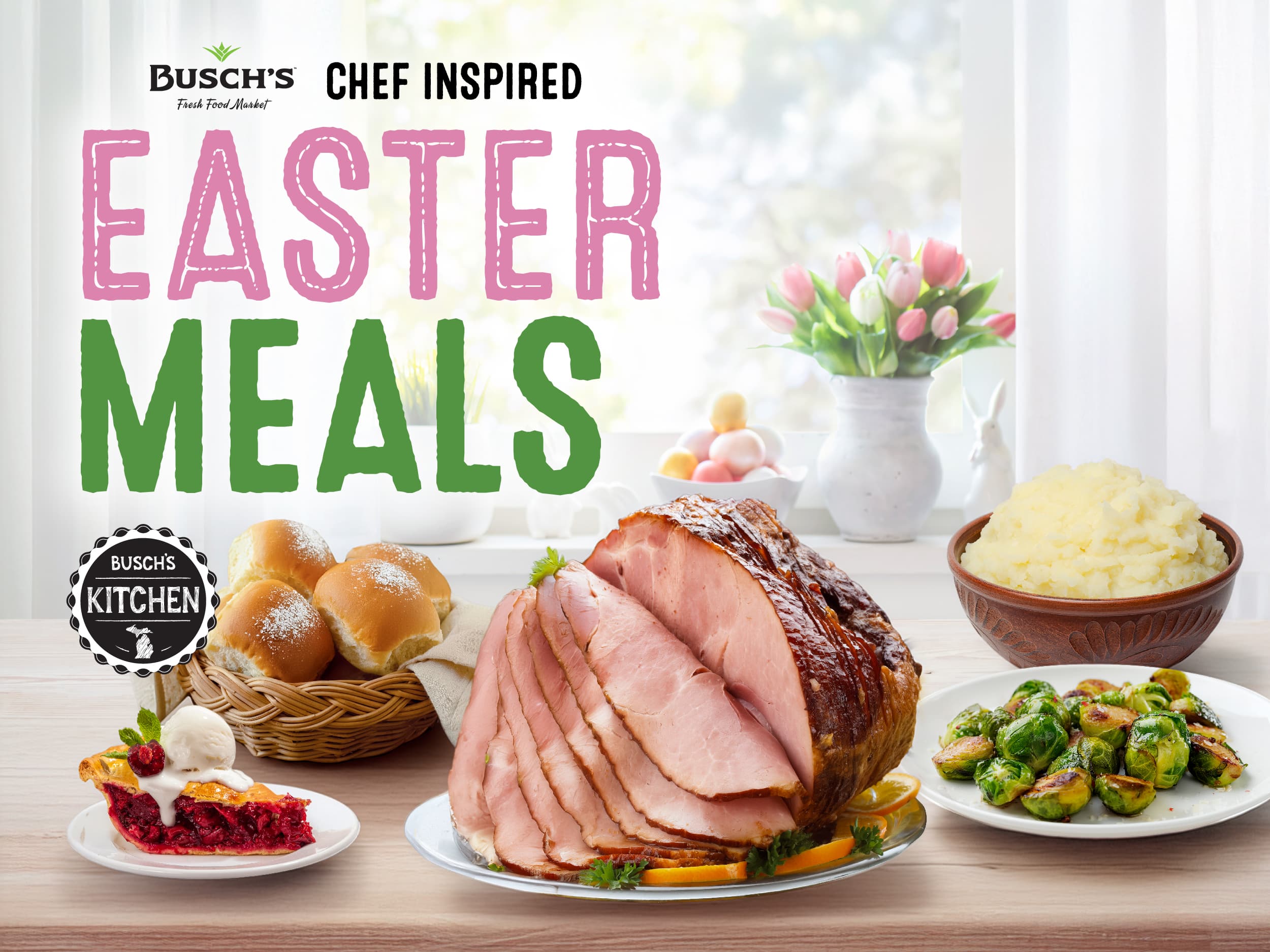 Easter meal spread featuring a glazed ham, mashed potatoes, Brussels sprouts, rolls, and pie. Pink tulips in the background convey a festive tone.