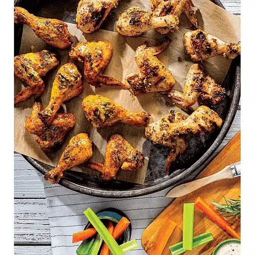 Grilled chicken wings on a parchment-lined tray, paired with carrots, celery, and a bowl of dip. A rustic, appetizing presentation.