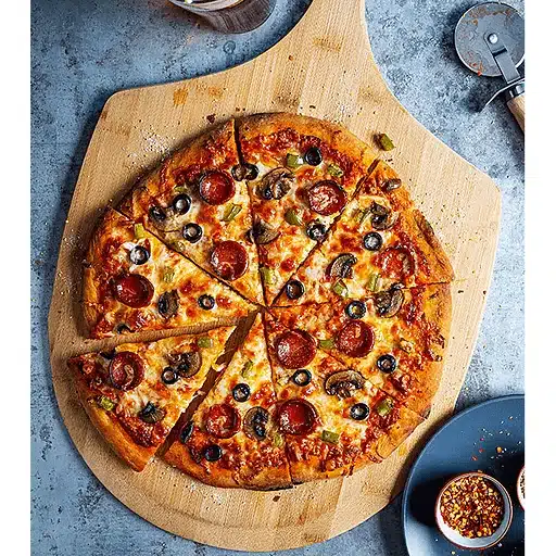 Pizza with pepperoni, olives, and mushrooms on a wooden board. A slice is removed. Nearby are red pepper flakes and a pizza cutter. Warm, inviting scene.