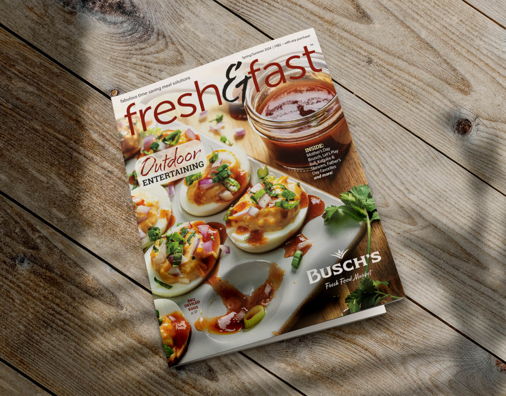 This is an image of a magazine titled "Fresh & Fast" resting on a wooden surface. The magazine cover features a photograph of a plate of beautifully arranged deviled eggs topped with vibrant garnishes, emphasizing outdoor entertaining. The cover also mentions "fabulous time-saving meal solutions" and includes the Busch's Fresh Food Market logo, indicating the magazine's affiliation with the grocery store. The overall layout is designed to appeal to readers interested in quick and easy gourmet recipes for social gatherings.
