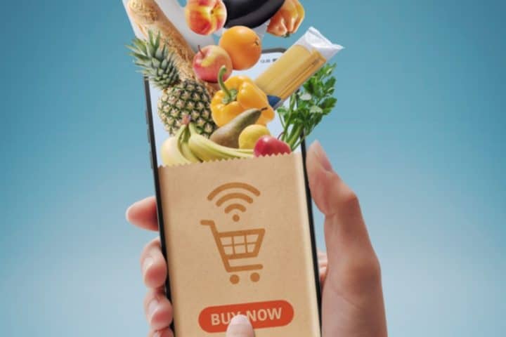 Person using smartphone for digital grocery shopping with fresh food items displayed