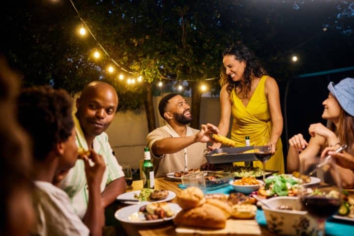 Group of people enjoying food together at outdoor gathering with string lights