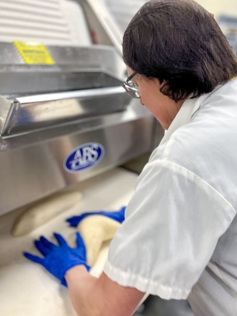 A woman in a white shirt and blue gloves kneads dough in a kitchen in Ann Arbor, Michigan