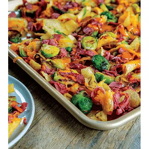 A colorful sheet pan filled with roasted Brussels sprouts, sweet potatoes, and corned beef, set on a rustic wooden table, conveying a cozy and hearty meal.