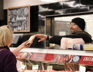 Image of an employee working at Busch's meat coutner handing a guest fresh meat product.