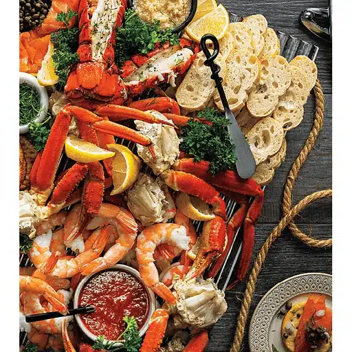 Platter of seafood with vibrant crab legs, shrimp, and lemon slices, garnished with parsley, accompanied by sliced bread and dipping sauces.