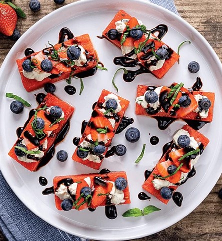 Watermelon appetizer bites topped with cheese, blueberries, and balsamic glaze