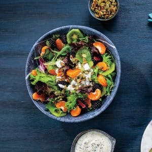 A colorful salad in a bowl accompanied by a separate bowl of dressing.