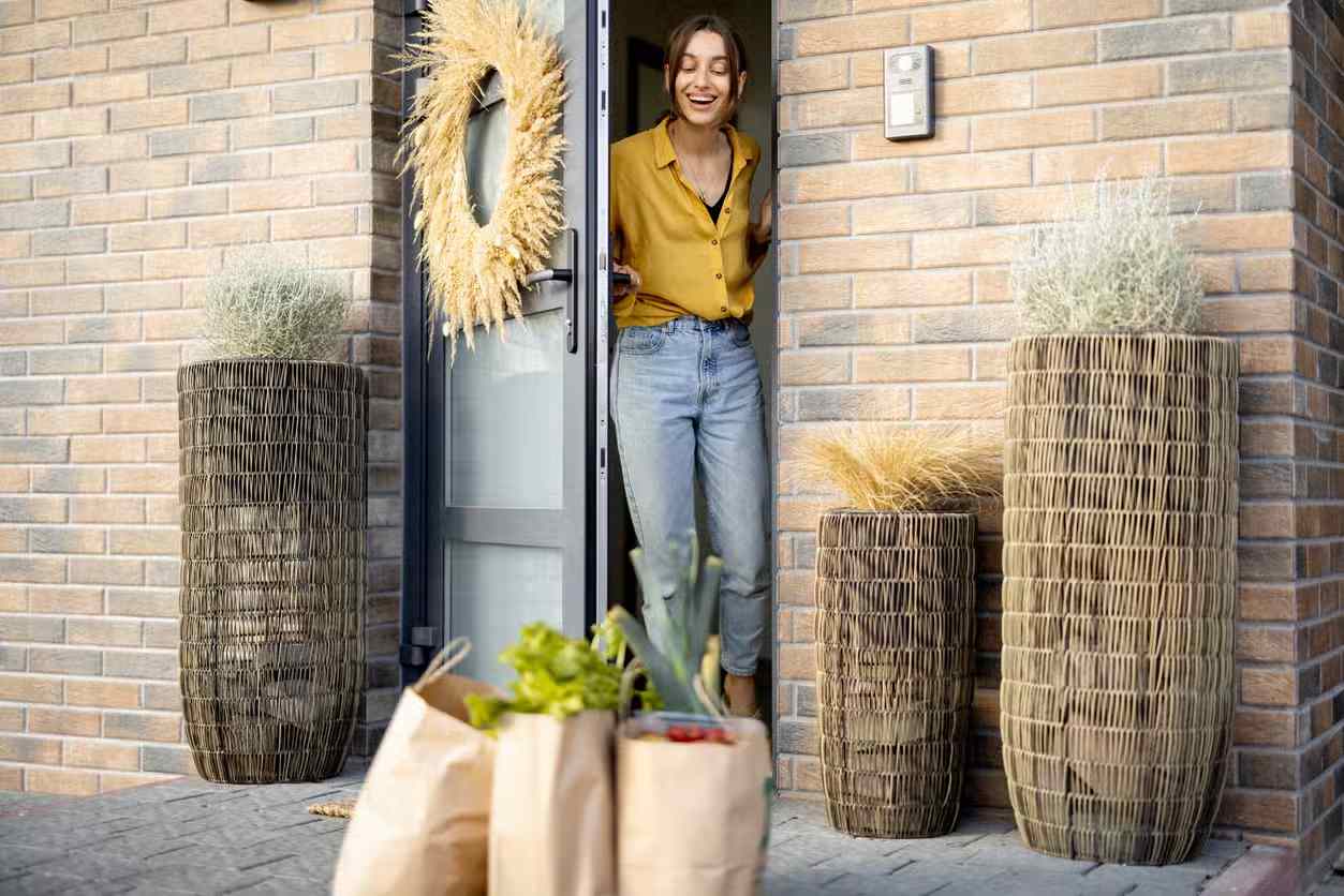 Person picking up grocery bags with fresh produce from doorstep in Ann Arbor, MI