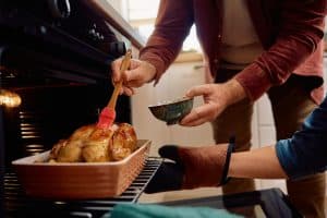 Close up of couple basting roast turkey while making Thanksgiving dinner in the kitchen.